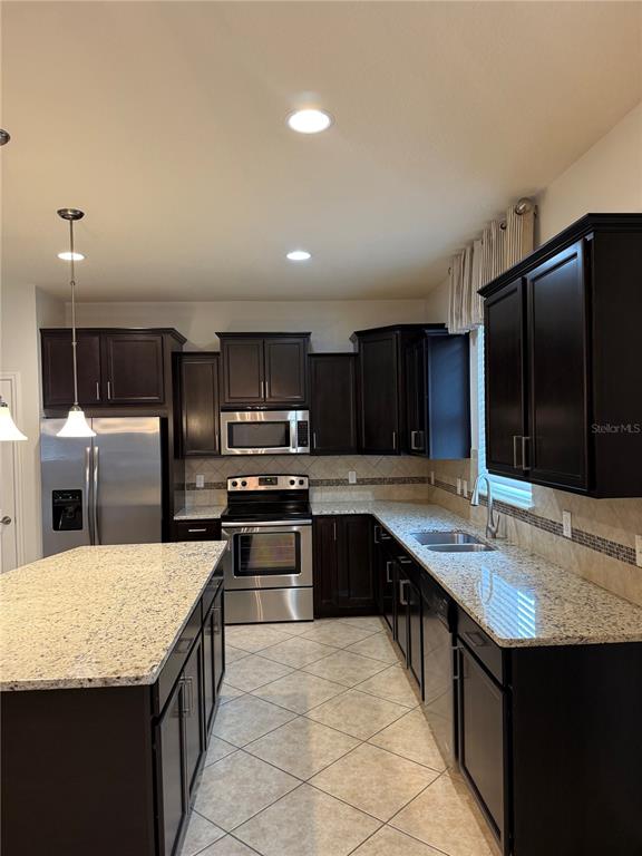 A kitchen with dark wood cabinets, granite countertops, stainless steel appliances, and tile flooring — 8519 RINDGE ROAD, POLK CITY, FL