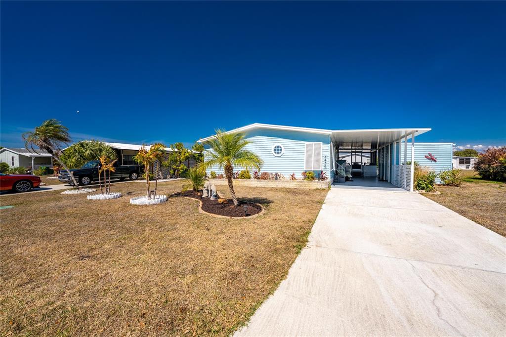 A light blue mobile home features a concrete driveway, a carport, and a landscaped yard — 8436 NIGHTHAWK DRIVE, ENGLEWOOD, FL