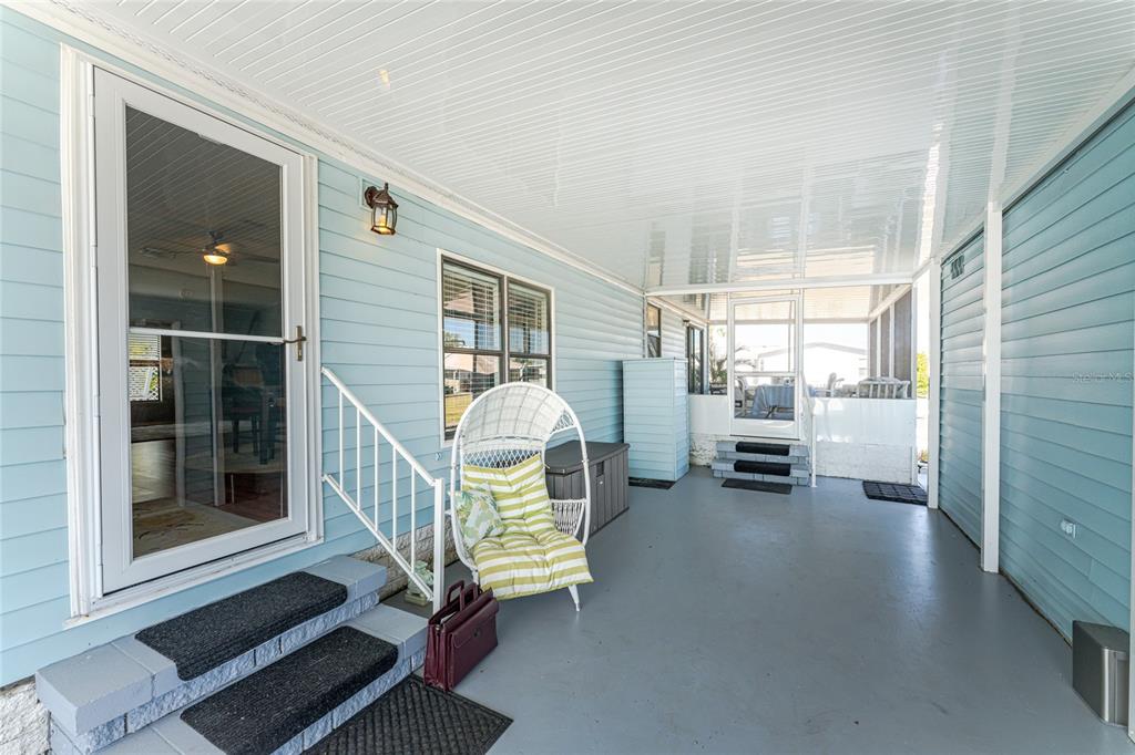 A covered patio with light blue siding, gray flooring, and a white wicker chair — 8436 NIGHTHAWK DRIVE, ENGLEWOOD, FL