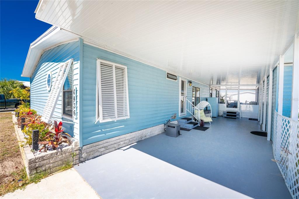 A light blue mobile home features a large covered carport and a concrete patio area — 8436 NIGHTHAWK DRIVE, ENGLEWOOD, FL