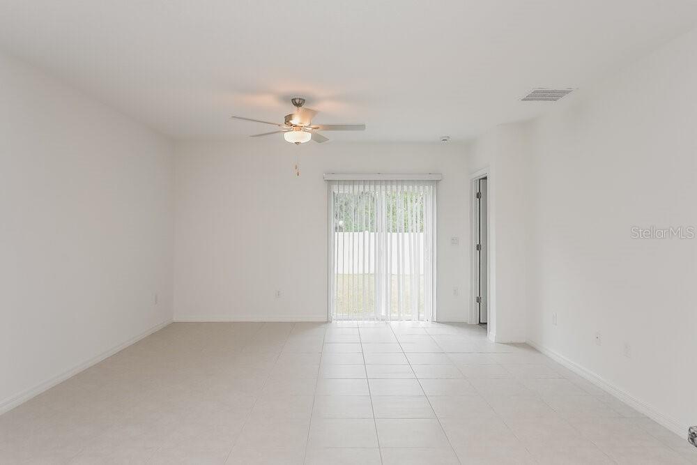 A bright, empty room features light-colored tile flooring, a ceiling fan, and sliding glass doors — 17954 BLISSFUL STARS DRIVE, LUTZ, FL