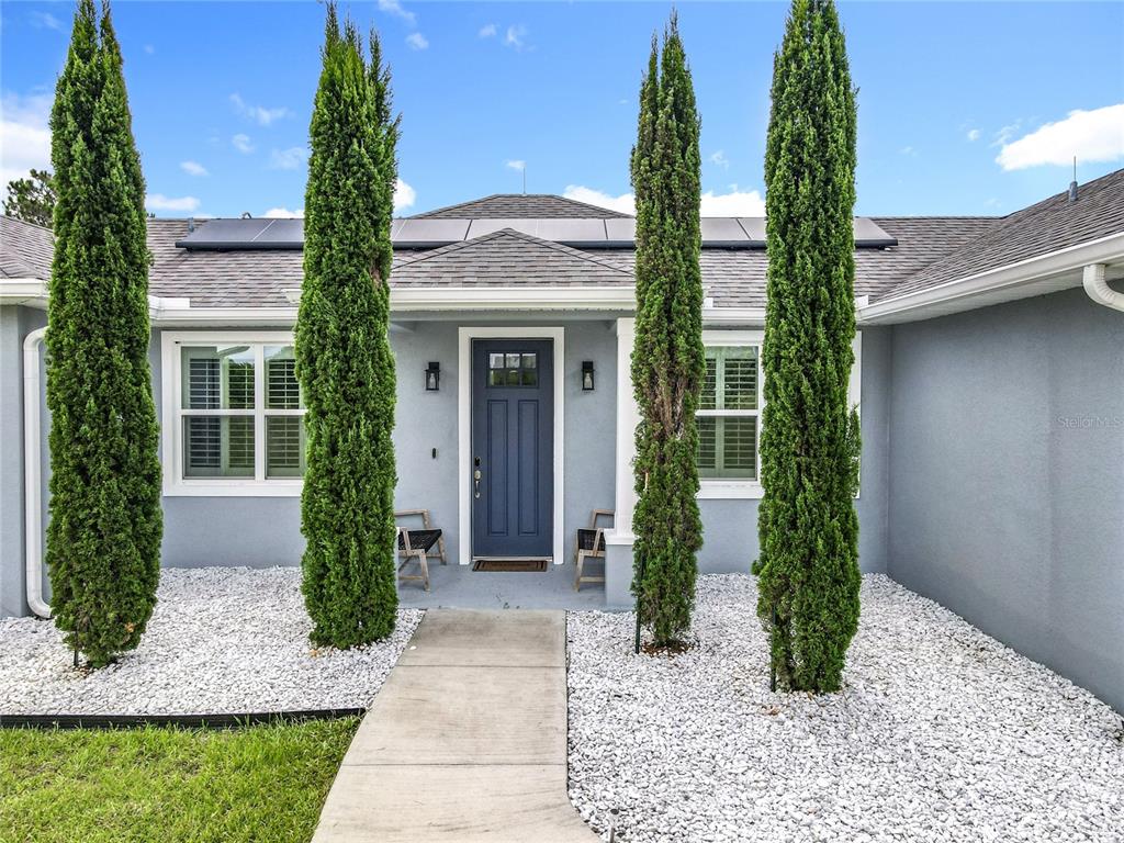 The front exterior of a gray house features a blue door and four tall cypress trees — 10220 BAY LAKE ROAD, GROVELAND, FL