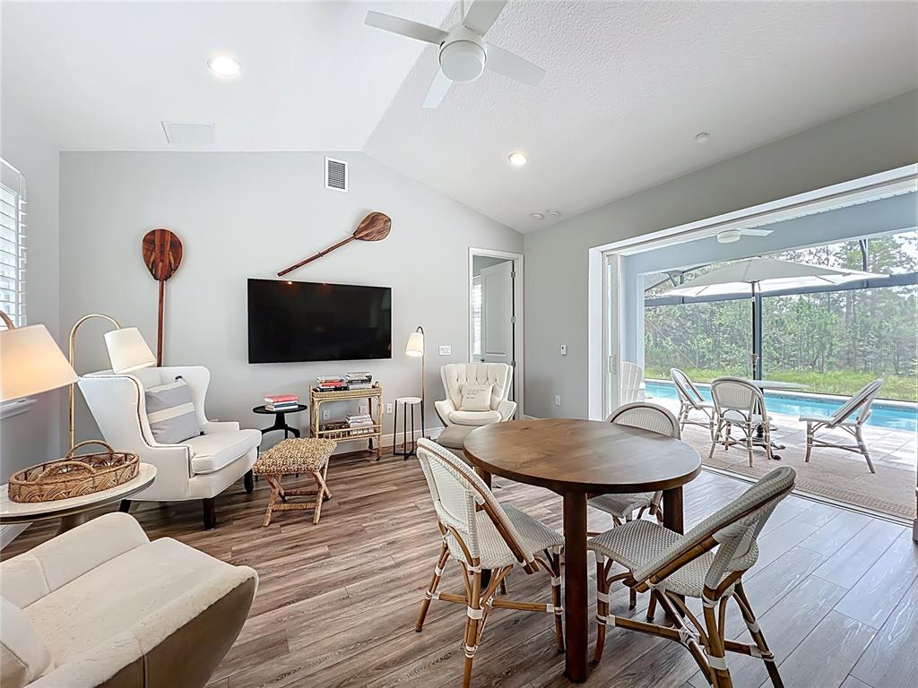 A living and dining area features a television, armchairs, a round table, and patio access — 10220 BAY LAKE ROAD, GROVELAND, FL