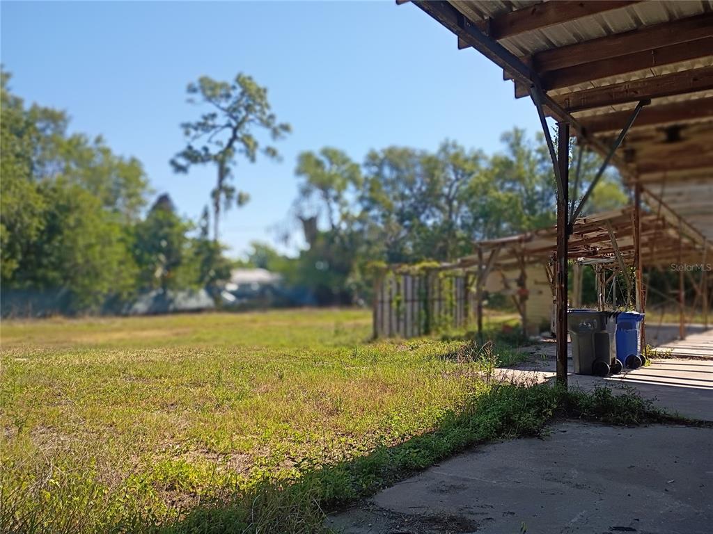 A grassy lot sits next to a covered outdoor structure with trash bins — 8615 NUNDY AVENUE, GIBSONTON, FL