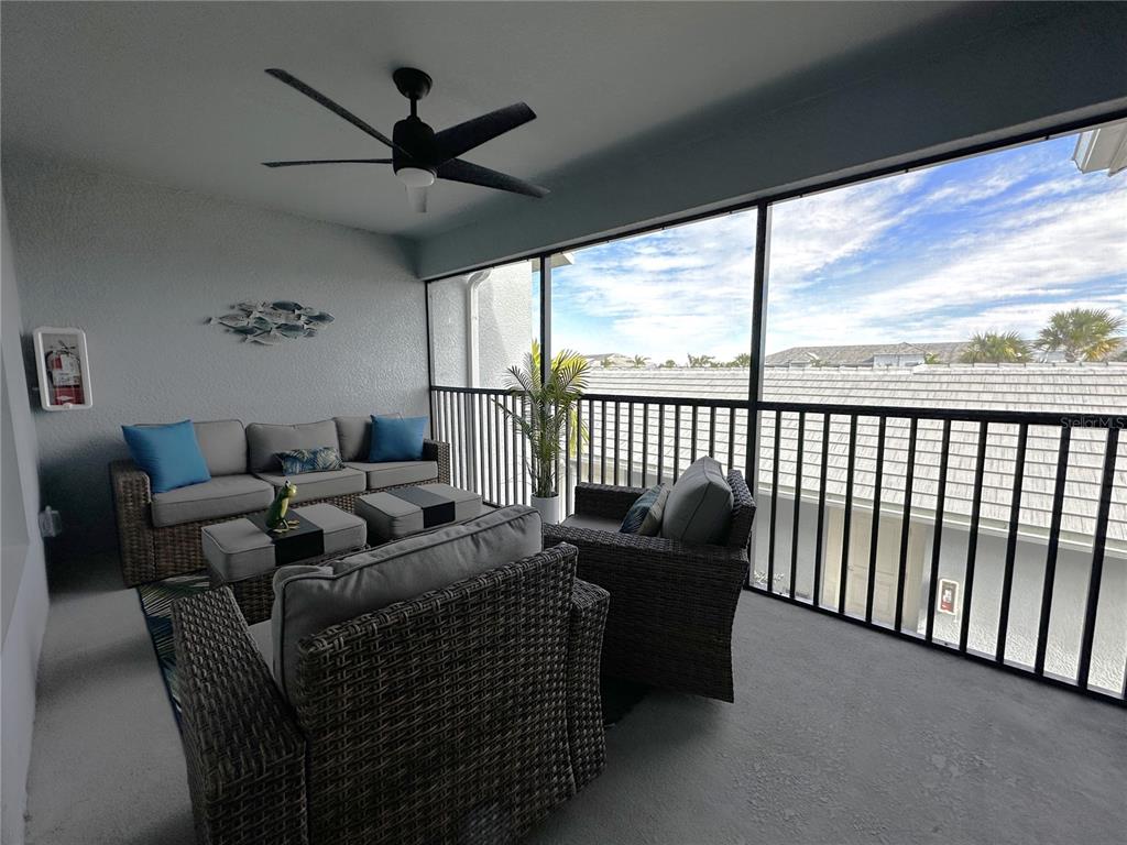A screened-in balcony features wicker patio furniture, a ceiling fan, and a view of rooftops — 14241 HERITAGE LANDING BOULEVARD UNIT 1821, PUNTA GORDA, FL