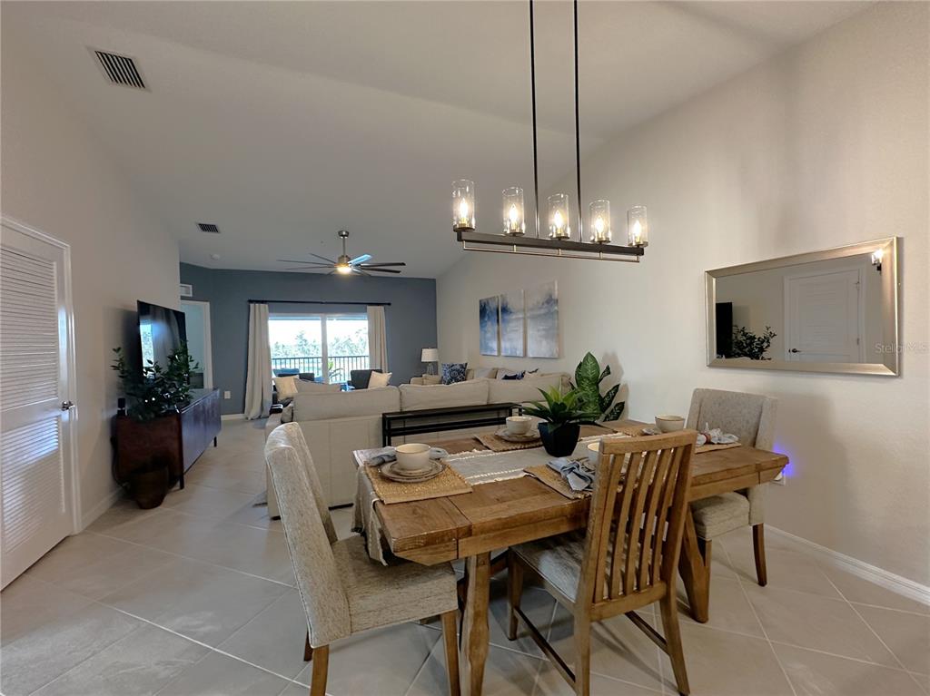 A dining area with a wooden table and light-colored chairs sits before an open living room — 14241 HERITAGE LANDING BOULEVARD UNIT 1821, PUNTA GORDA, FL
