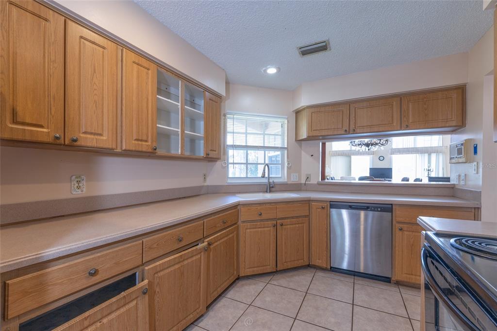 A kitchen features oak cabinets, laminate countertops, a stainless steel dishwasher, and tile flooring — 29 CHEROKEE COURT W, PALM COAST, FL