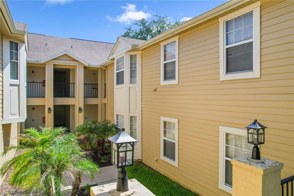 An exterior view of a multi-story apartment building with yellow siding and a courtyard — 425 SUMMIT RIDGE PLACE UNIT 211, LONGWOOD, FL