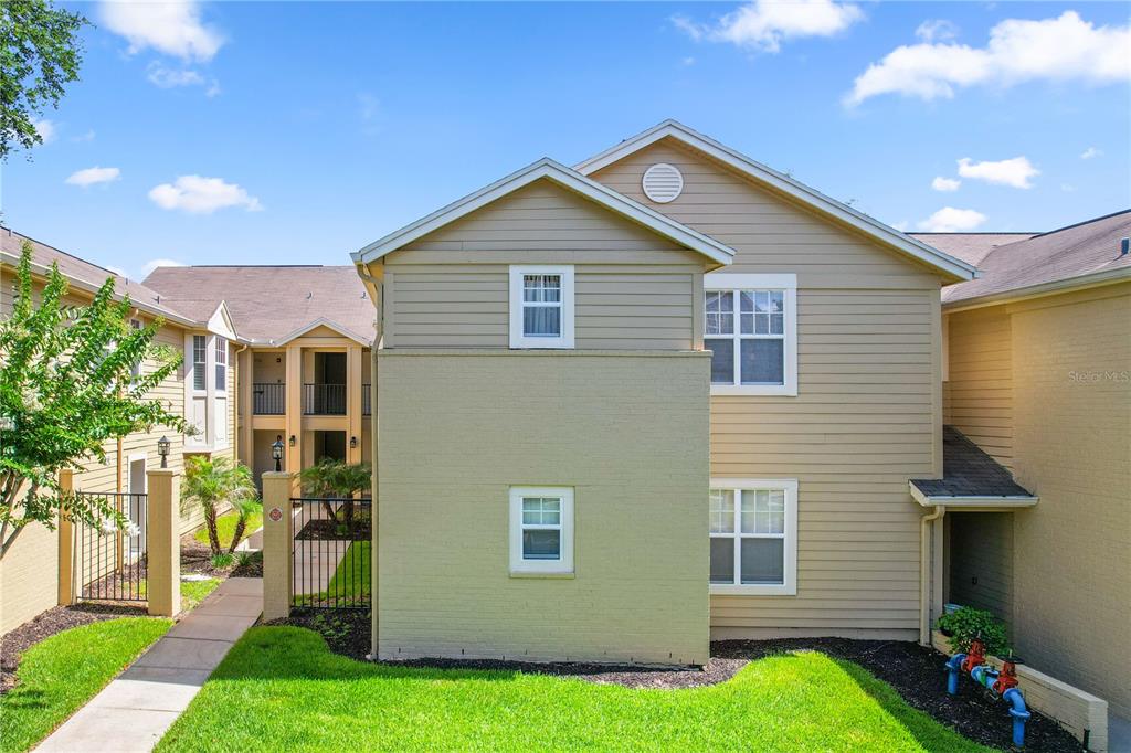 The exterior of a multi-story apartment building features tan siding and a green lawn — 425 SUMMIT RIDGE PLACE UNIT 211, LONGWOOD, FL