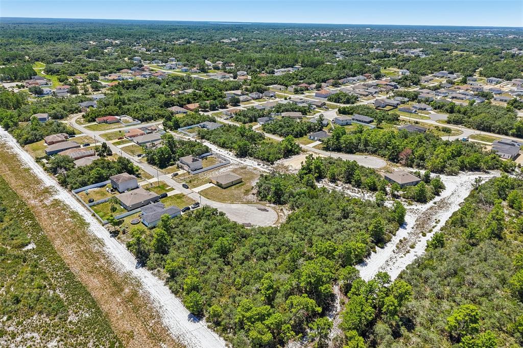 An aerial view shows a suburban neighborhood with houses, paved roads, and surrounding wooded areas — 1249 ALAFIA WAY, POINCIANA, FL