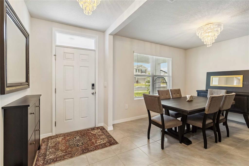 A dining room with tile floors, a dark wood table, and two crystal chandeliers — 18006 CANOPY PLACE, BRADENTON, FL