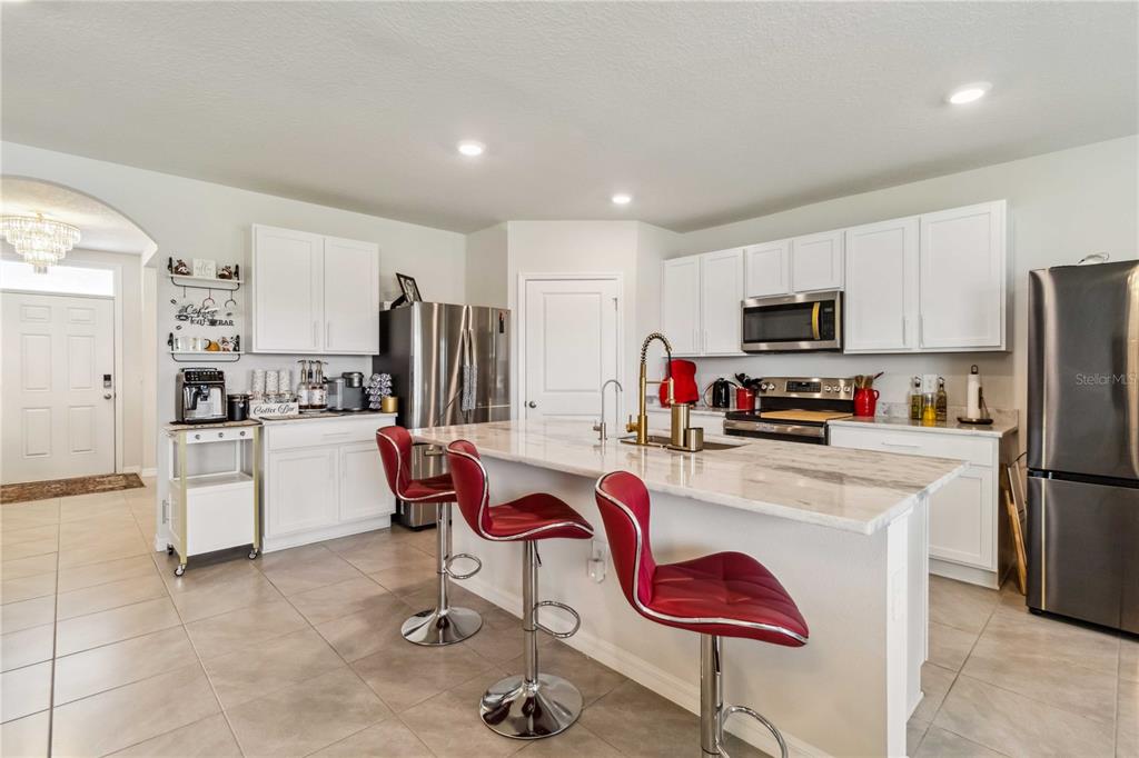 A kitchen features white cabinetry, a marble-topped island with red barstools, and stainless steel appliances — 18006 CANOPY PLACE, BRADENTON, FL