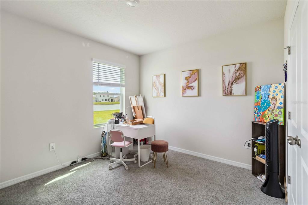 A bedroom with a desk, a window, wall art, and a small bookshelf on carpet — 18006 CANOPY PLACE, BRADENTON, FL