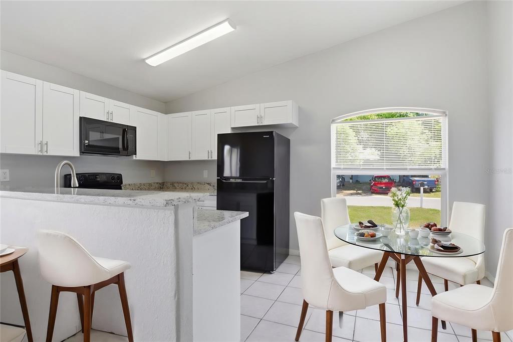A kitchen with white cabinets and granite countertops sits beside a dining area with chairs — 6018 FLORA TERRACE, APOLLO BEACH, FL