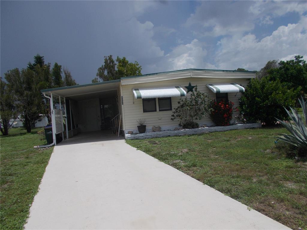 A single-story mobile home features a concrete driveway, a carport, and two window awnings — 6872 HAAWI COURT, NORTH PORT, FL