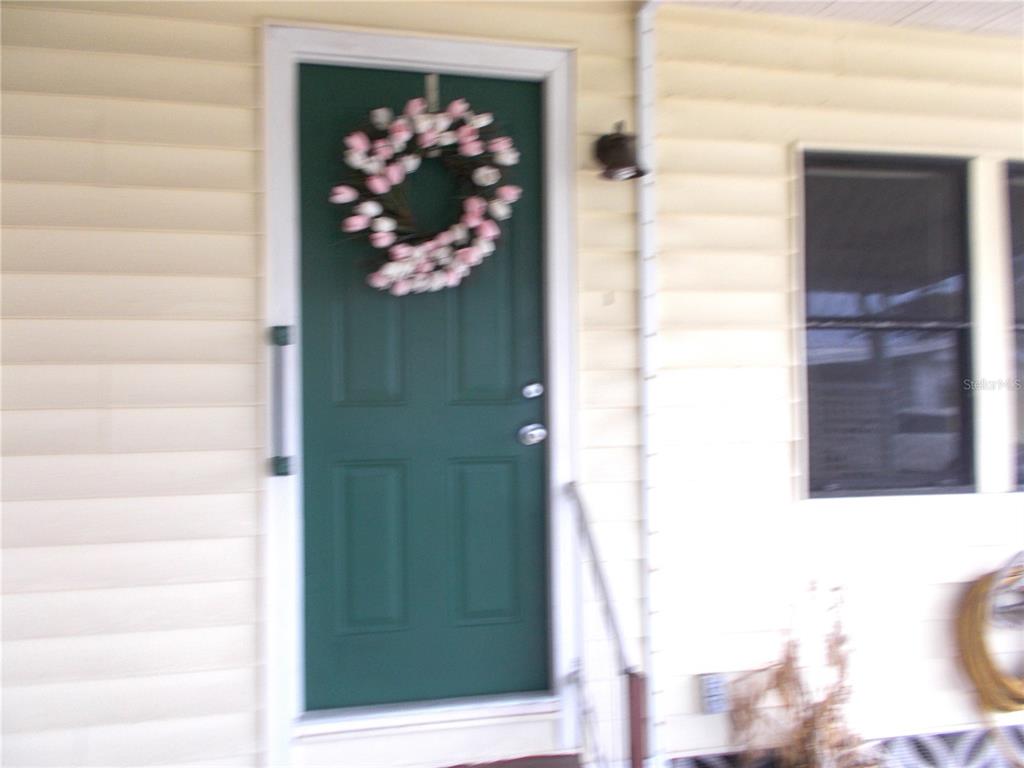 A green front door with a floral wreath is set into light-colored horizontal siding — 6872 HAAWI COURT, NORTH PORT, FL