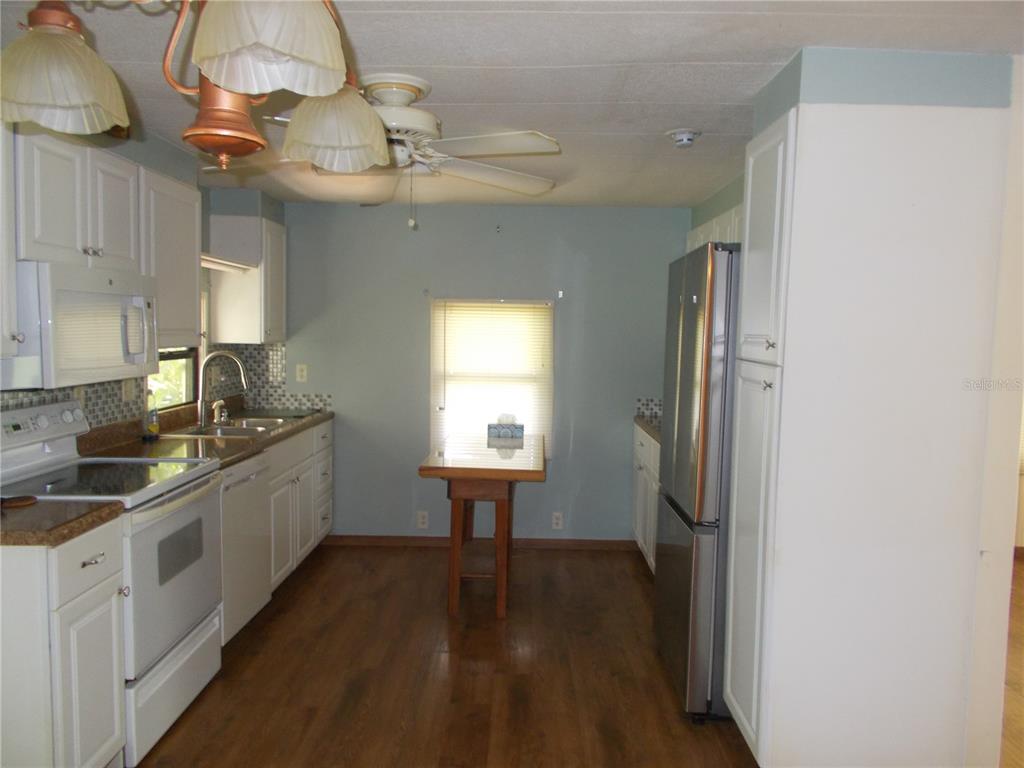 A kitchen with white cabinets, stainless steel appliances, wood-look flooring, and a small dining table — 6872 HAAWI COURT, NORTH PORT, FL