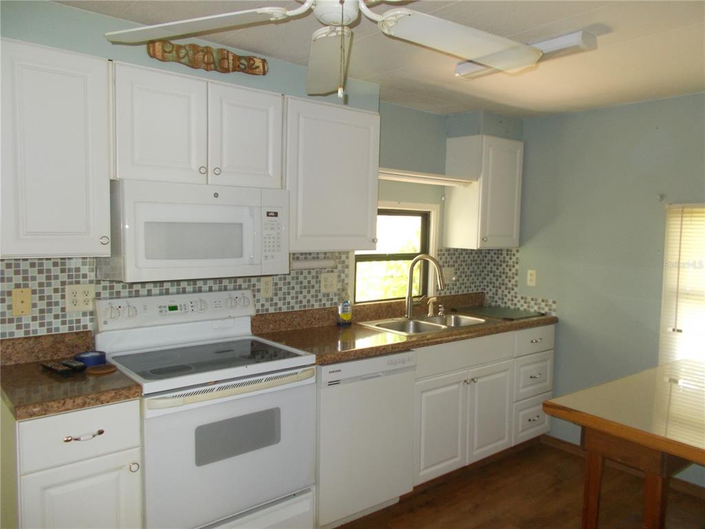 A kitchen features white cabinets, a white stove, a dishwasher, and a mosaic tile backsplash — 6872 HAAWI COURT, NORTH PORT, FL
