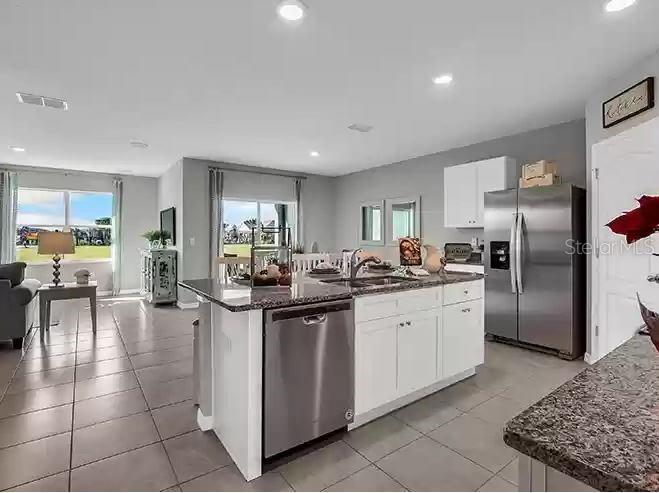 A kitchen with a stainless steel dishwasher, granite countertops, and white cabinets opens to a living area — 3820 SWANFALLS TERRACE, SANFORD, FL