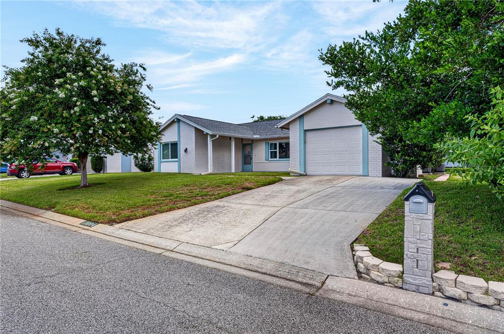 A single-story house with a white brick exterior, a concrete driveway, and a front lawn — 13004 SERPENTINE DRIVE, HUDSON, FL
