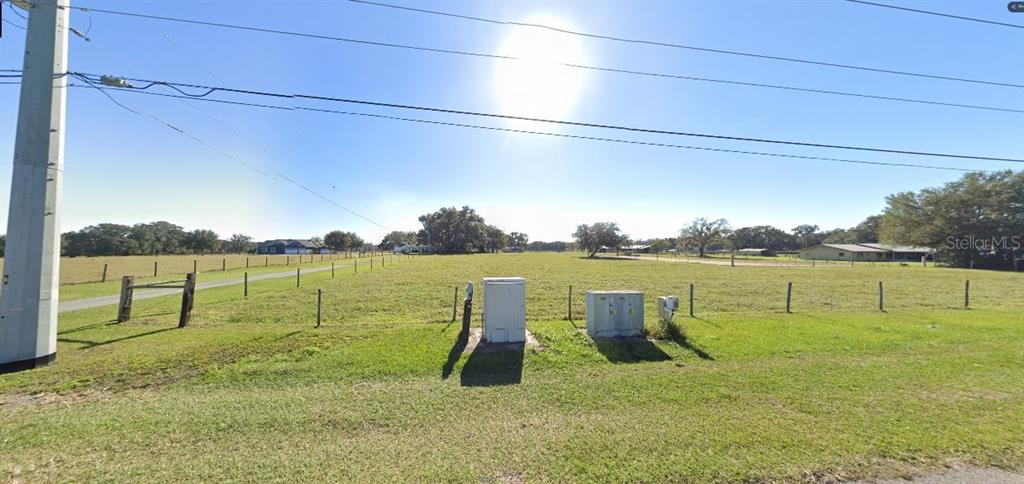 A wide, grassy, fenced-in vacant lot is viewed from the roadside under a bright sun — OLD POLK CITY RD, POLK CITY, FL