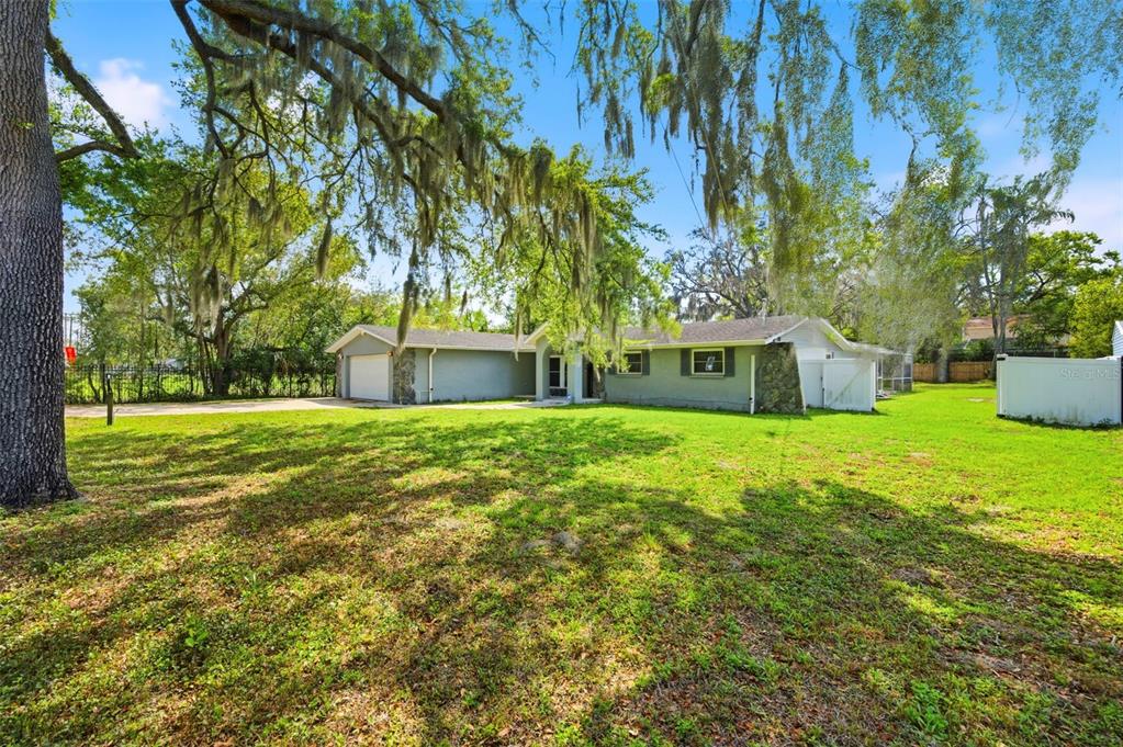 A single-story house with a gray exterior, stone accents, and a large, tree-shaded front yard — 212 W 131ST AVENUE, TAMPA, FL