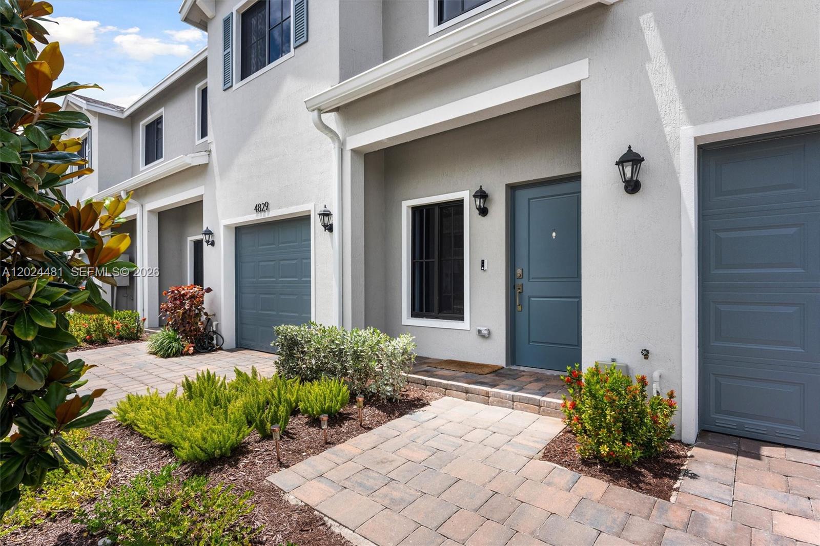 The exterior of a two-story townhouse features a gray facade, blue garage doors, and landscaping — 4825 Dillion St, Lake Worth FL 33463, LAKE WORTH, FL