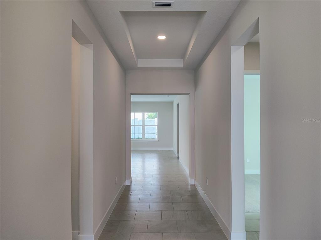 A hallway with tile flooring leads to a room with a window and tray ceiling — 776 ANEGADA LANE, SARASOTA, FL