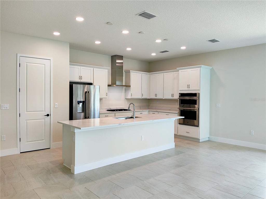 A modern kitchen features white cabinets, stainless steel appliances, and a large marble-topped island — 776 ANEGADA LANE, SARASOTA, FL