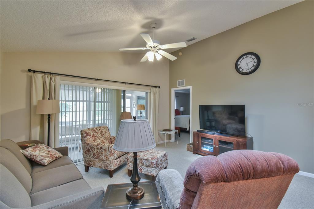 A living room features a vaulted ceiling, a ceiling fan, a television, and sliding glass doors — 5247 NW 18TH STREET, OCALA, FL