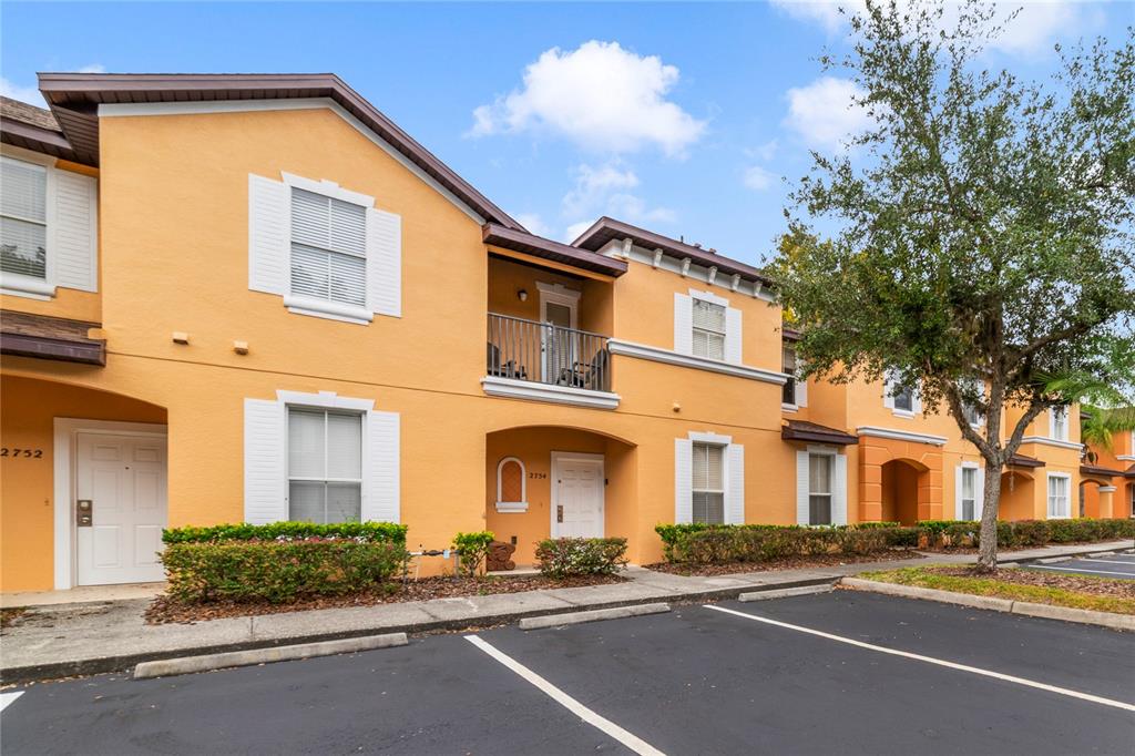 A two-story orange stucco apartment building features white trim, a balcony, and parking spaces — 2754 CORVETTE LANE, KISSIMMEE, FL