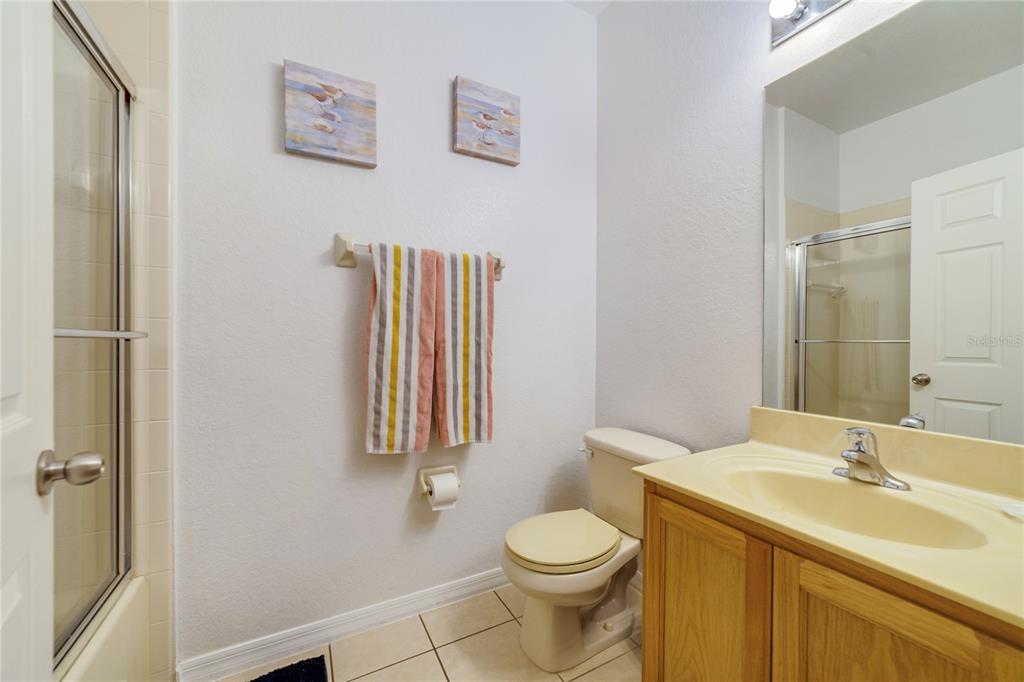 A bathroom features a wooden vanity, a beige toilet, a shower stall, and wall art — 2754 CORVETTE LANE, KISSIMMEE, FL