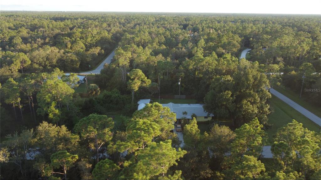 An aerial view shows a house nestled among dense trees near two intersecting paved roads — 28153 ALATADENA DRIVE, PUNTA GORDA, FL