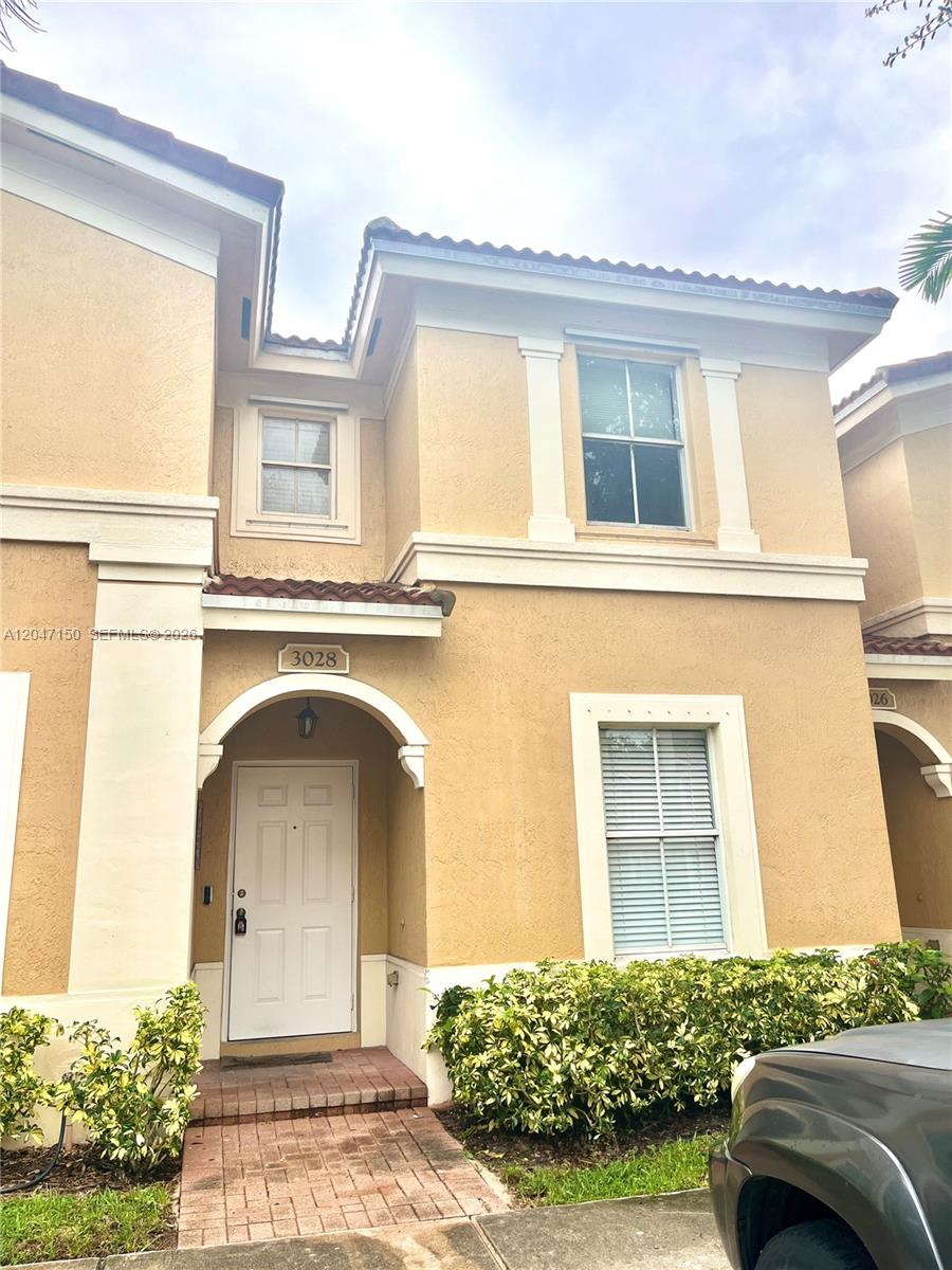 A two-story tan stucco townhouse features a white front door and a brick walkway — 3028 SW 129th Ter # 120, Miramar FL 33027, MIRAMAR, FL