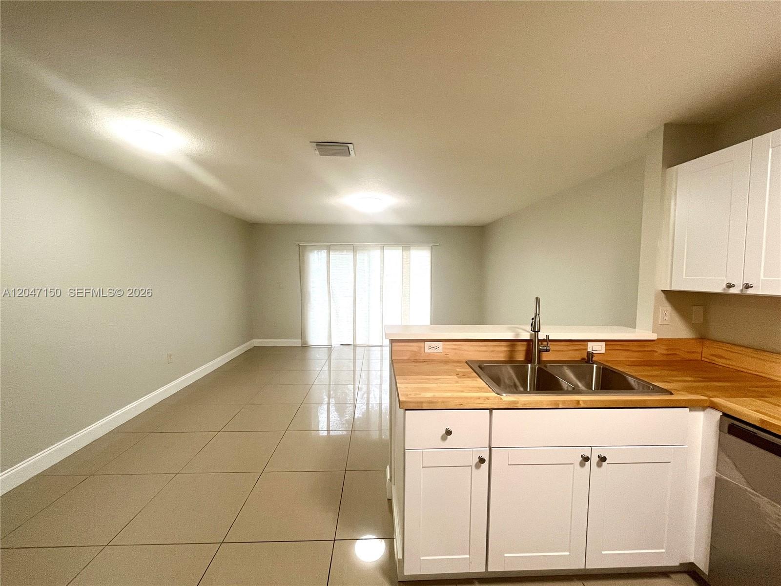 A kitchen with white cabinets and wood countertops overlooks an open-concept living area with tile floors — 3028 SW 129th Ter # 120, Miramar FL 33027, MIRAMAR, FL