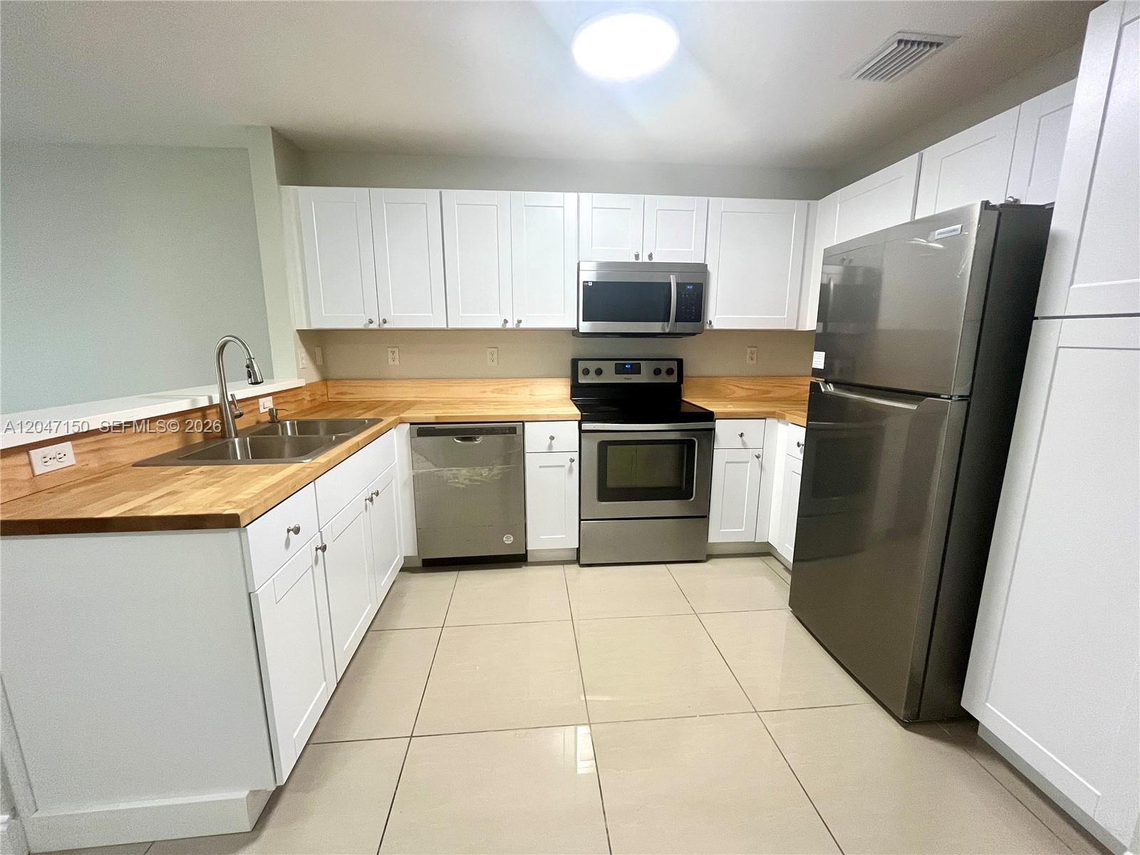 A kitchen features white cabinets, stainless steel appliances, and light wood countertops over tile floors — 3028 SW 129th Ter # 120, Miramar FL 33027, MIRAMAR, FL