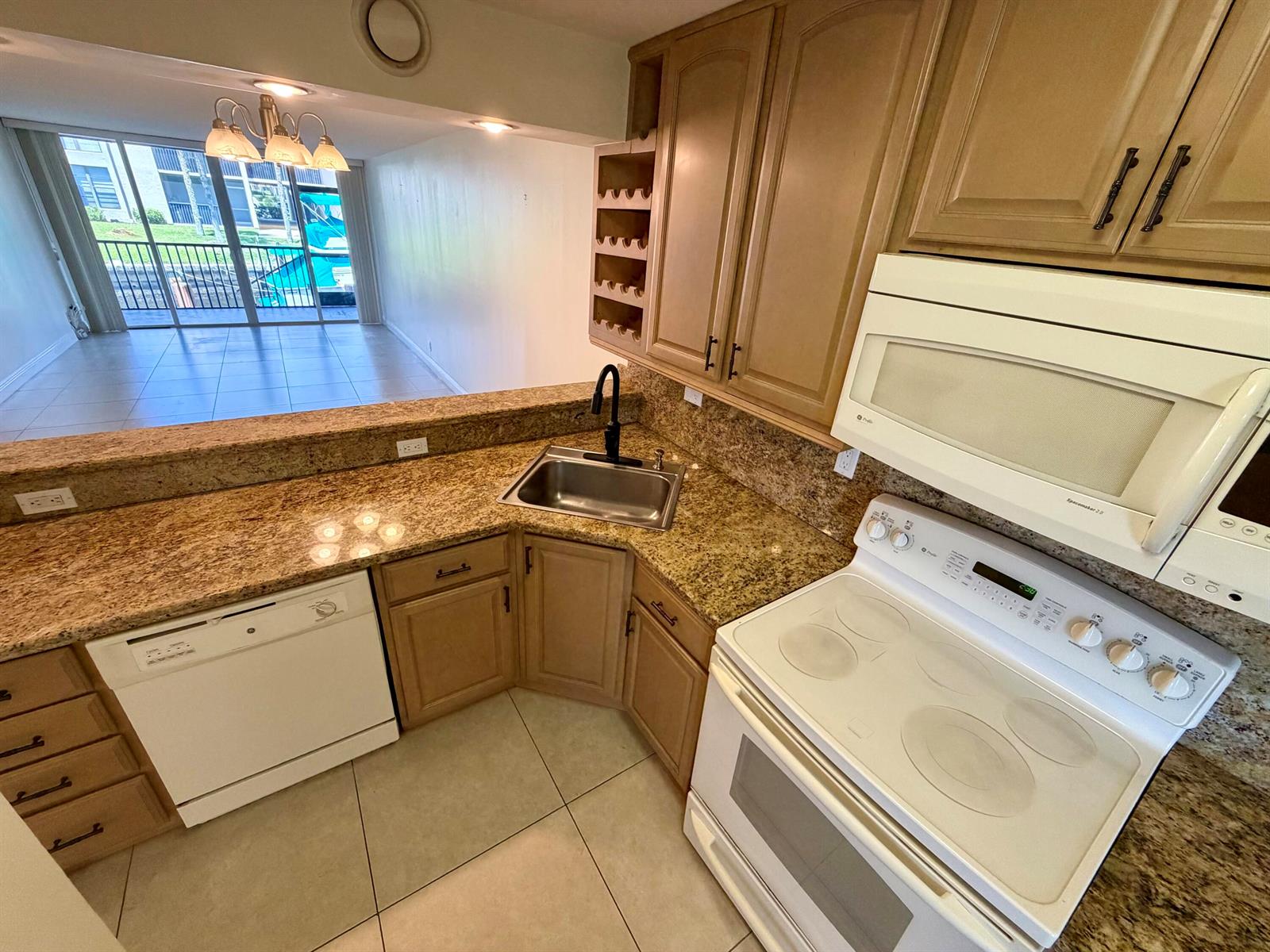 A kitchen with light wood cabinets, granite countertops, white appliances, and a view of a balcony — 6 Royal Palm Way # 102, Boca Raton FL 33432, BOCA RATON, FL