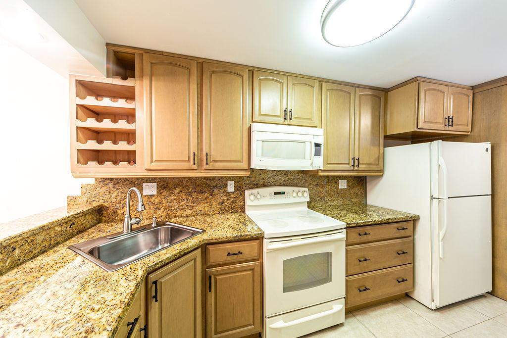 A kitchen features light wood cabinets, granite countertops, a white stove, and a white refrigerator — 6 Royal Palm Way # 102, Boca Raton FL 33432, BOCA RATON, FL