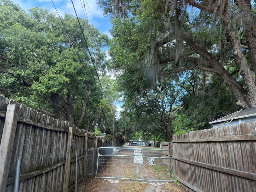 A metal gate blocks a dirt path between two wooden fences under large trees — 1257 LYNCHBURG ROAD, LAKE ALFRED, FL