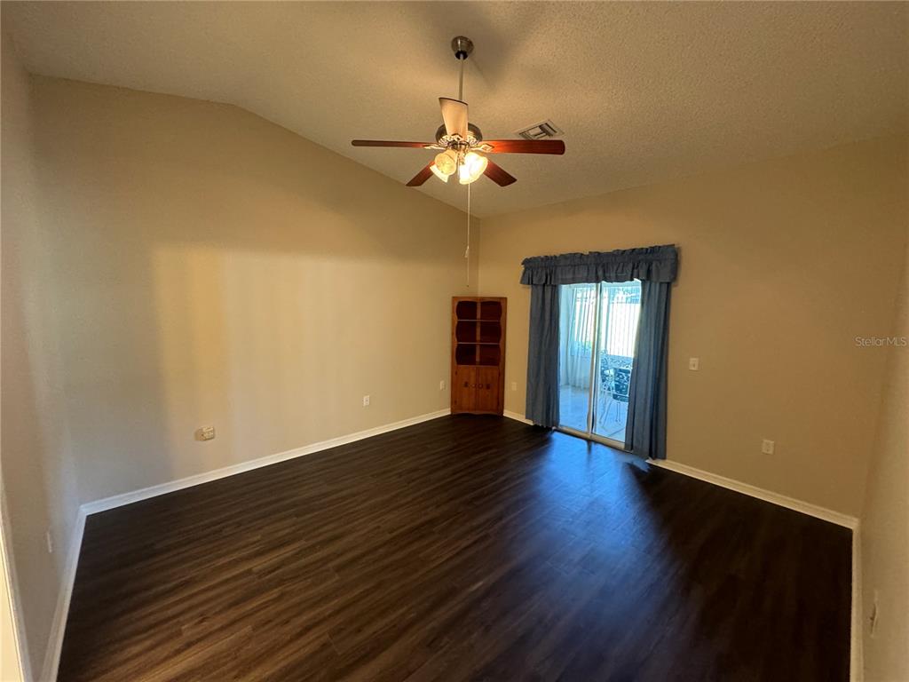 A living room features dark wood-look flooring, a ceiling fan, and sliding glass patio doors — 545 GOLFVIEW COURT, LEESBURG, FL