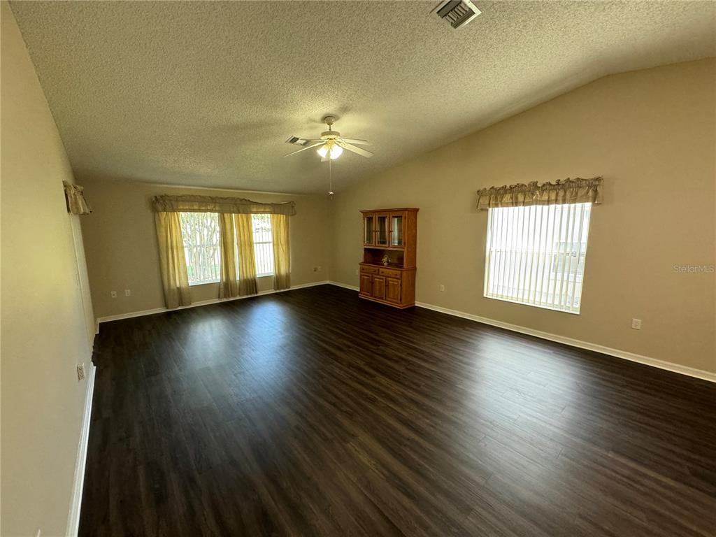 A living room with dark wood-look flooring, vaulted ceilings, a ceiling fan, and a hutch — 545 GOLFVIEW COURT, LEESBURG, FL