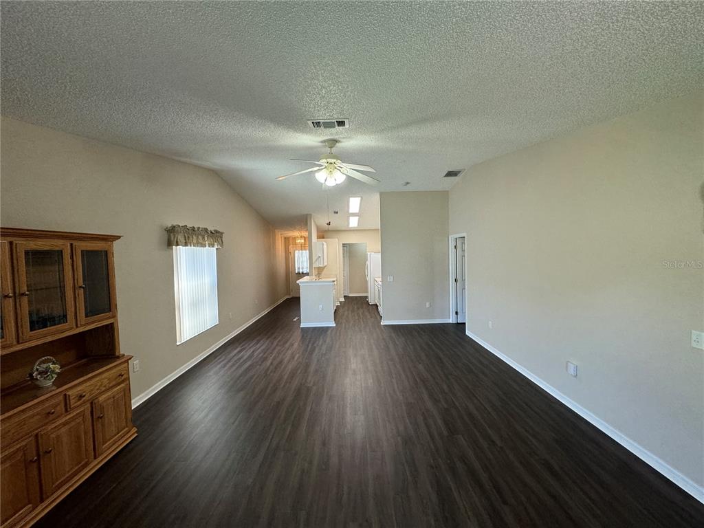 A living room with dark wood-look flooring, a vaulted ceiling, and an open kitchen beyond — 545 GOLFVIEW COURT, LEESBURG, FL