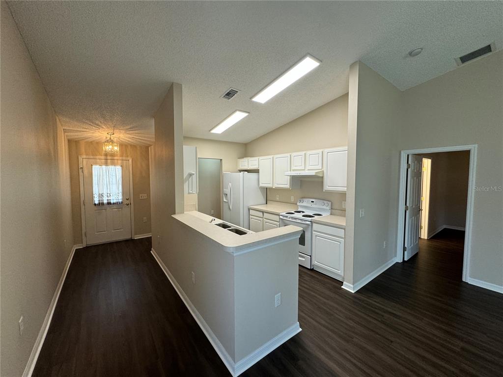 A kitchen with white cabinets and appliances features a breakfast bar overlooking a living area — 545 GOLFVIEW COURT, LEESBURG, FL