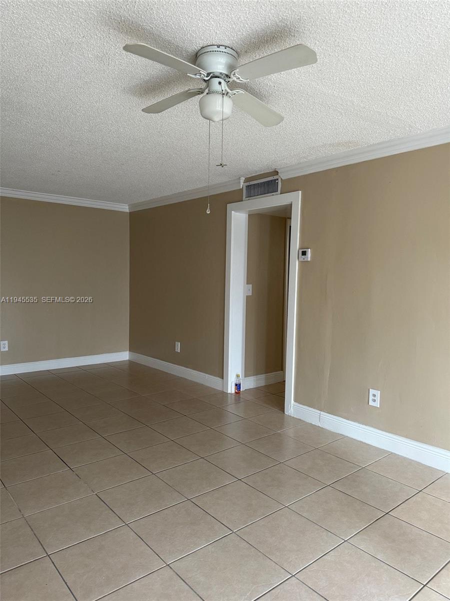 An empty room features beige walls, a popcorn ceiling, a ceiling fan, and tiled floors — 488 NW 165th St Rd # 115, Miami FL 33169, MIAMI, FL