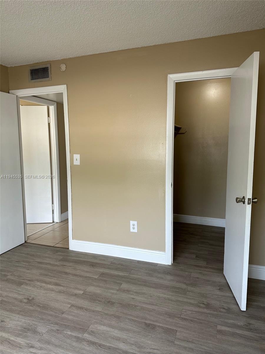 A room with tan walls, wood-look flooring, and two open doorways leading to other spaces — 488 NW 165th St Rd # 115, Miami FL 33169, MIAMI, FL