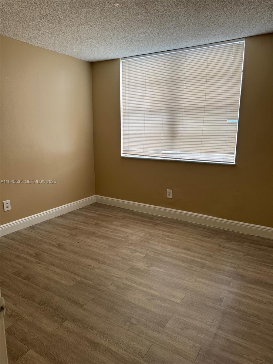 An empty bedroom features tan walls, light wood-look flooring, and a window with closed blinds — 488 NW 165th St Rd # 115, Miami FL 33169, MIAMI, FL