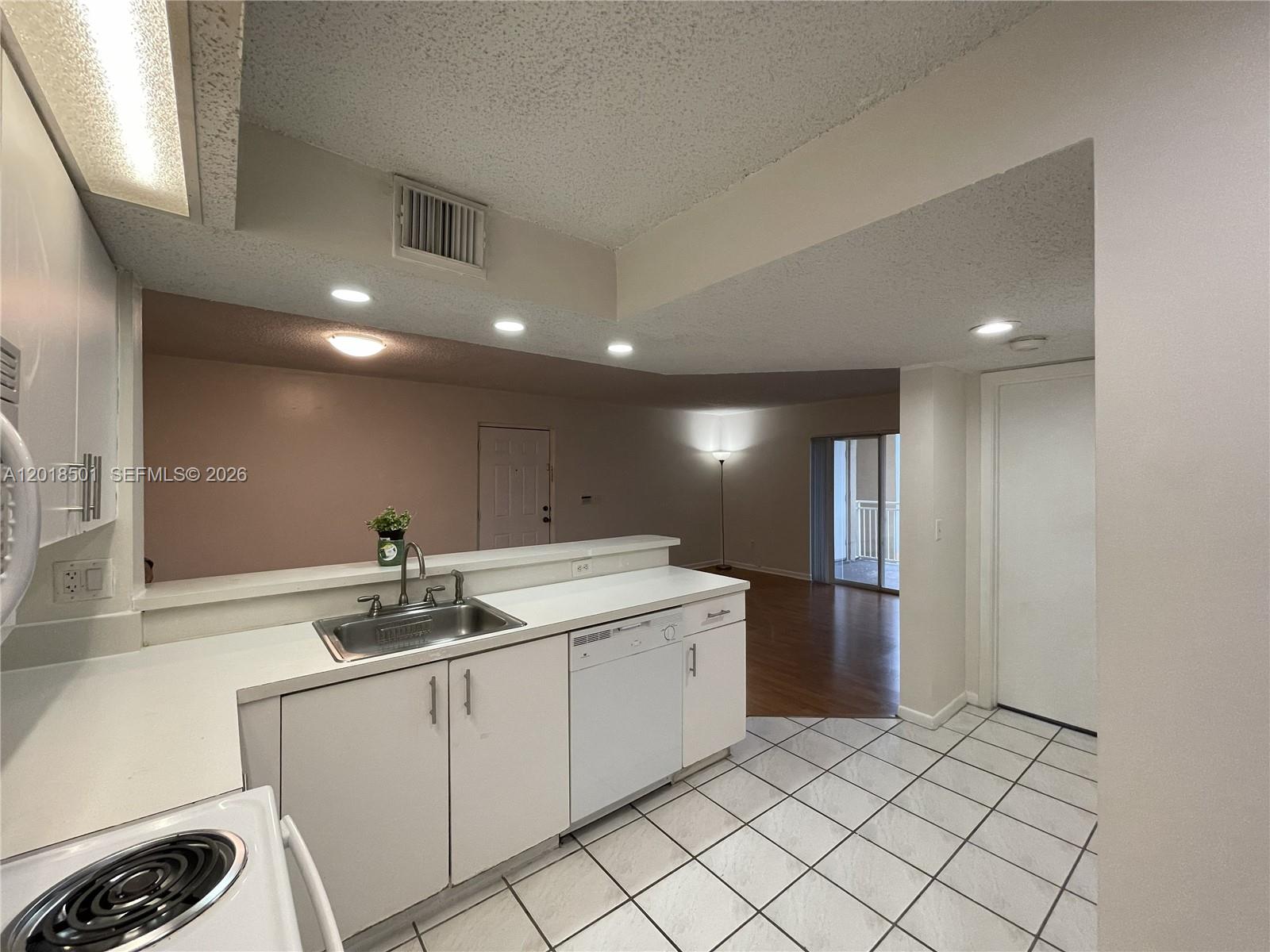 A kitchen with white cabinets, a stainless steel sink, and tile flooring overlooks a living area — 18890 NW 57th Ave # 207, Hialeah FL 33015, HIALEAH, FL