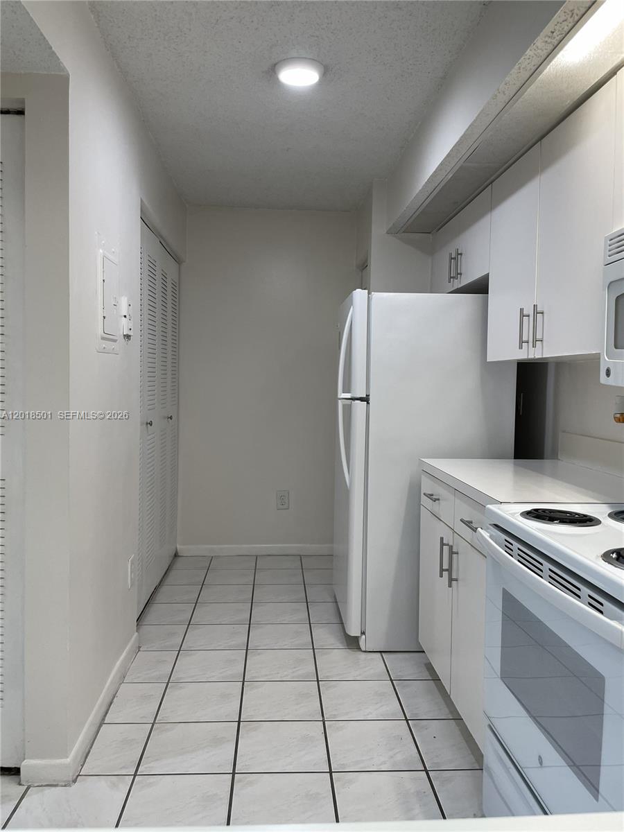 A narrow kitchen features white cabinets, white appliances, and light-colored tiled flooring — 18890 NW 57th Ave # 207, Hialeah FL 33015, HIALEAH, FL