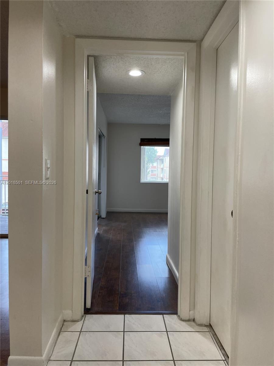A hallway with white tile flooring leads into a room with dark wood-look flooring — 18890 NW 57th Ave # 207, Hialeah FL 33015, HIALEAH, FL