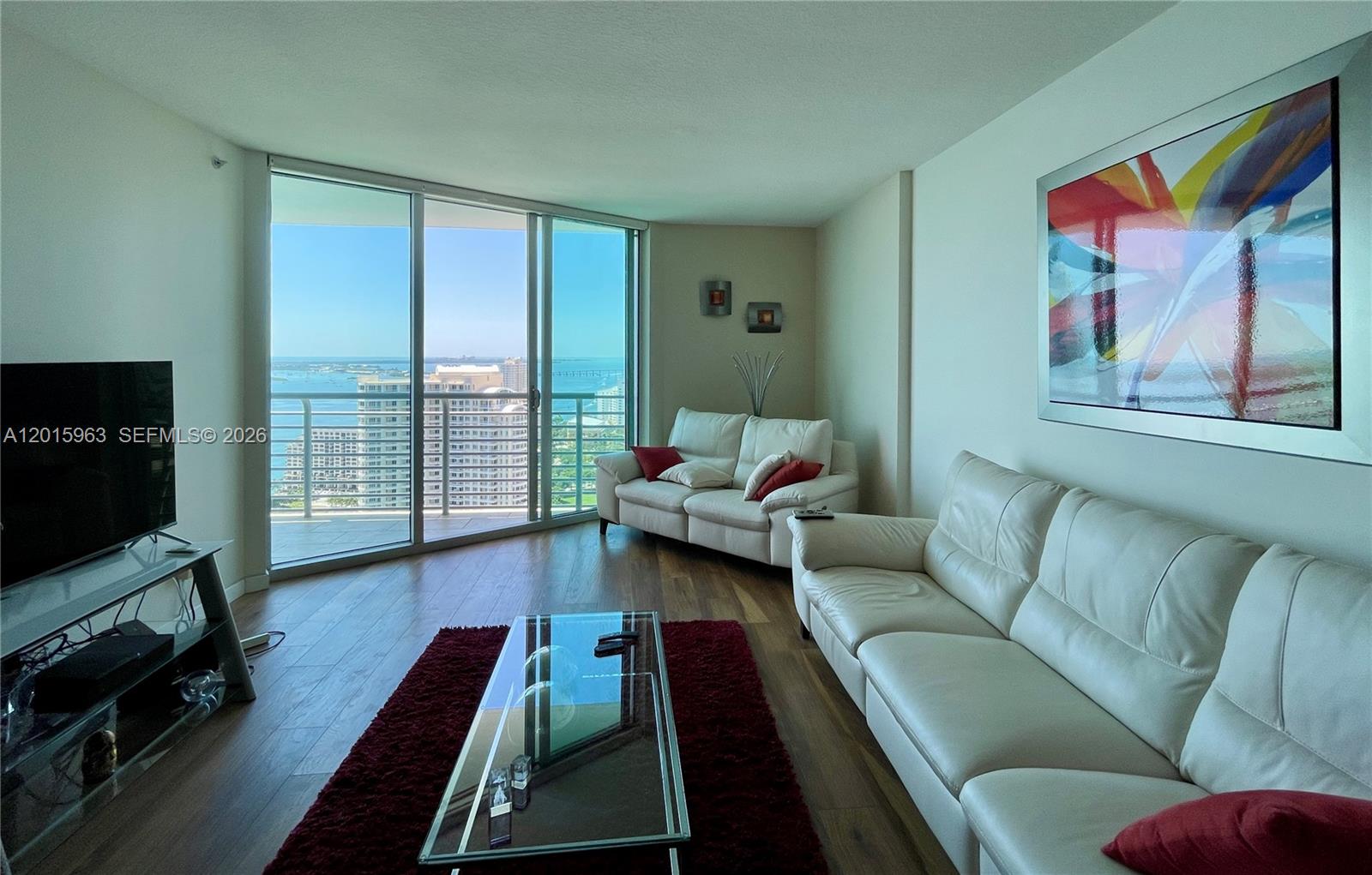 A living room features white leather sofas, a glass coffee table, and floor-to-ceiling windows — 335 S Biscayne Blvd # 3603, Miami FL 33131, MIAMI, FL